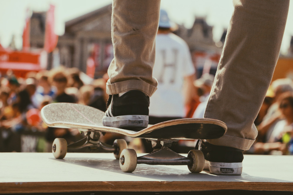 vue sur les pieds d'un homme portant un chino beige et des baskets foncées un pied sur un skate